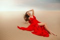 Sexy elegant stylish woman model lies posing on summer desert. Red luxury silk trendy long dress. Beautiful bare legs