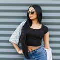 Sexy elegant young hipster woman in stylish sunglasses with long gorgeous hair in a trendy T-shirt in a summer jacket in jeans Royalty Free Stock Photo