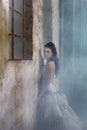fantasy bride leaning agaisnt rustic wall surrounded by fog