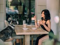 Sexy fantasy woman sitting at table with cup coffee in hand. Offers tasty drink to dog. Bullterrier looks at its Royalty Free Stock Photo