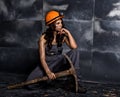 female miner worker with pickaxe, in coveralls over his naked body, sitting on the floor on backdrop of steel wall Royalty Free Stock Photo