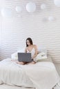 Caucasian girl in sexy silk lingerie works on a laptop while sitting in bed. Vertical photo. Royalty Free Stock Photo