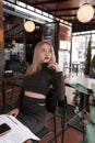 Sexy girl blonde in black clothes in cafe. Young woman relaxes in the cafeteria. Vertical frame