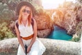 A sexy girl in a hat with a backpack enjoys an incredibly beautiful view of a stone bridge over the gorge Fiordo di Furore. Little