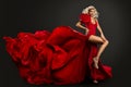 Sexy Girl in Red Silk Dress flying on Wind. Fashion Blond Woman in Long Luxury Slit Gown flying on Wind. Glamour Model Wavy Hair Royalty Free Stock Photo