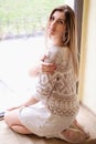 Sexy girl sitting on the big window in cafe. single women in beige knitted sweater