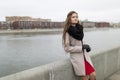 girl standing on the waterfront in the fall. Girl in a black coat, a scarf and a red dress against a gray sky. Not Isolated.