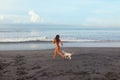 Sexy Girl. Tanned Woman Running On Sandy Beach. Beautiful Brunette In Bikini Playing With Dog Royalty Free Stock Photo