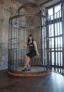 Sexy gothic girl in tight black dress behind the big cage posing as slavery victim alone