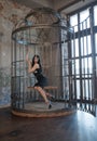 Sexy gothic girl in tight black dress behind the big cage posing as slavery victim alone