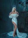 Sexy, gothic, snow queen in a white vintage dress posing with a bare leg. A blonde girl in a crown with icicles on a Royalty Free Stock Photo