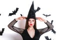 Happy gothic young woman in witch halloween costume with hat standing and smiling over white background