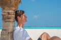 Sexy handsome model man in stylish clothes relaxing under palm tree at tropical sandy beach at island luxury resort Royalty Free Stock Photo