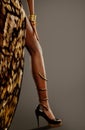Sexy Leg in High Heels Shoes in Golden Dress. Black Skin Model Hand with Gold Jewelry Bracelets and Bangle over Dark background. Royalty Free Stock Photo