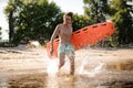 long-haired beach lifeguard running in water with life-savi