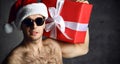 Sexy man hold red christmas present gift box in new year santa hat with naked torso in sunglasses Royalty Free Stock Photo