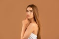 Millennial woman with long straight hair touching her face, having soft healthy skin and nude makeup on brown background Royalty Free Stock Photo