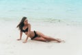 model in black swimsuit lying on white sandy beach. Girl sunbathes and rests on vacation at tropical island Royalty Free Stock Photo