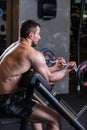 Sexy muscular man sitting on the bench and doind biceps exercise. Side view Royalty Free Stock Photo
