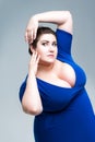 Sexy plus size fashion model in blue dress with deep neckline, fat woman on gray background, body positive concept