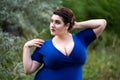 Sexy plus size fashion model in blue dress with a deep neckline outdoors, beautiful fat woman with big breasts in nature