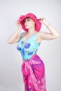 Sexy plus size girl in a blue swimsuit, fuchsia hat with brim and in a trendy bright pareo stands on a white background in the Stu Royalty Free Stock Photo