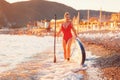 Sexy plus sized woman in red bikini walking down the beach holding a sup board and paddle. The concept of sports and Royalty Free Stock Photo