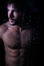 Sexy portrait of handsome naked man with beard, blue eyes and sixpack abs in rainfall shower looking at camera