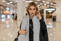 Sexy pretty stylish young blond woman with gray eyes in a luxurious gray coat with a vintage scarf with a fashionable bag Royalty Free Stock Photo
