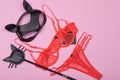 Sexy red womens underwear and set of erotic toys for BDSM. The game of sexual slavery with a leather whip and mask on a light pink Royalty Free Stock Photo