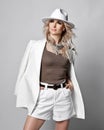 Sexy rich blonde woman in white wide-brimmed stetson hat, shorts and jacket on shoulders stands looking aside Royalty Free Stock Photo