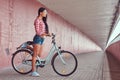 stylish brunette girl wearing a pink flannel shirt and denim shorts in glasses, posing with city bike against a Royalty Free Stock Photo