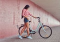 stylish brunette girl wearing a pink flannel shirt and denim shorts in glasses, posing with city bike against a Royalty Free Stock Photo