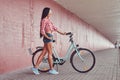 stylish brunette girl wearing a pink flannel shirt and denim shorts in glasses, posing with city bike against a Royalty Free Stock Photo