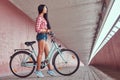 stylish brunette girl wearing a pink flannel shirt and denim shorts in glasses, posing with city bike against a Royalty Free Stock Photo