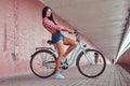 stylish brunette girl wearing a pink flannel shirt and denim shorts in glasses, posing with city bike against a Royalty Free Stock Photo