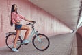 stylish brunette girl wearing a pink flannel shirt and denim shorts in glasses, posing with city bike against a Royalty Free Stock Photo