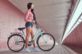 stylish brunette girl wearing a pink flannel shirt and denim shorts in glasses, posing with city bike against a Royalty Free Stock Photo