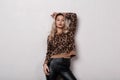 Sexy stylish young woman with curly blond hair in fashionable leopard sweater in fashionable black leather pants posing in a