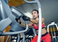 and sweaty Asian woman training hard at gym using elliptical pedaling machine gear in intense workout