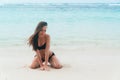 tanned girl in black swimsuit posing on sandy beach near ocean. Beautiful model sunbathes and rests Royalty Free Stock Photo