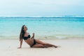 tanned girl in black swimsuit posing on sandy beach near ocean. Beautiful model sunbathes and rests Royalty Free Stock Photo