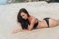 tanned girl in black swimsuit posing on sandy beach near ocean. Beautiful model sunbathes and rests Royalty Free Stock Photo