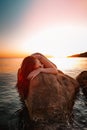 Sexy tanned woman posing lying on her stomach, on the coastal rocks. Sea and sunset in the background. Vertical orientation Royalty Free Stock Photo