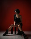 Sexy thoughtful woman in black tight dress, leather jacket and big brutal boots sitting on a fallen stepladder on red Royalty Free Stock Photo