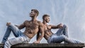 Sexy torso attractive body. Denim pants emphasize masculinity sexuality. Men twins brothers muscular guys sit relax sky