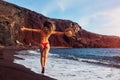 Sexy woman in bikini relaxing on Red beach in Santorini, Greece. Girl running and jumping, having fun