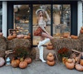 Sexy woman with blond hair in elegant autumn outfit posing in decorated cafe with a lot of pumpkins