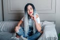 Sexy woman with dreadlocks. Hand near the face, pensive look. White t-shirt and blue jeans. Sitting on a gray sofa. Studio photo Royalty Free Stock Photo