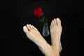 Girl feet of ideal beauty with Mortons toe on black, soft cared skin and toes with white nail polish, red rose in glass vase Royalty Free Stock Photo